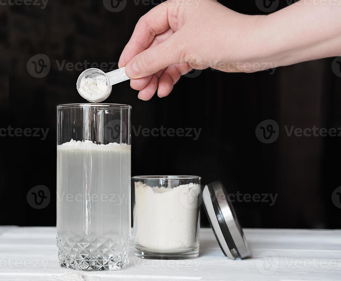 mulher de mão feminina fazendo bebida de proteína de soro de leite em um copo e jarra com proteína em pó. suplemento para articulações saudáveis e beleza. vista de corte, coquetel dietético vegano foto