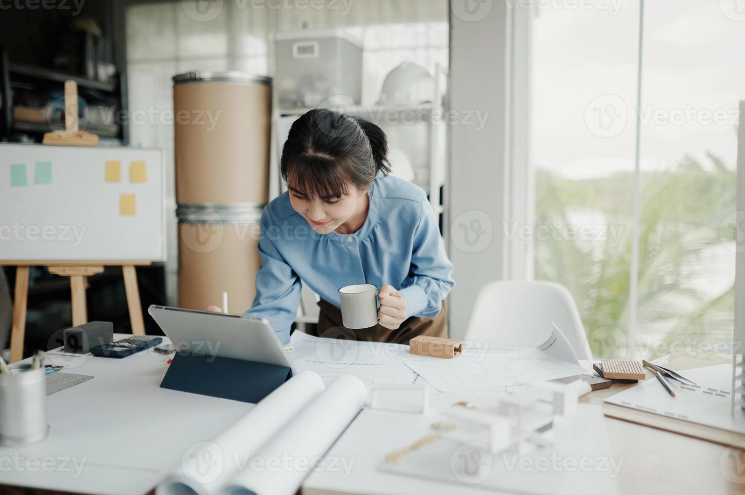 foco seletivo, arquiteta ou engenheira asiática desenhando o design do interior do edifício usando um tablet. arquiteta ou engenheira asiática senta e analisa, projeta projetos no escritório. foto