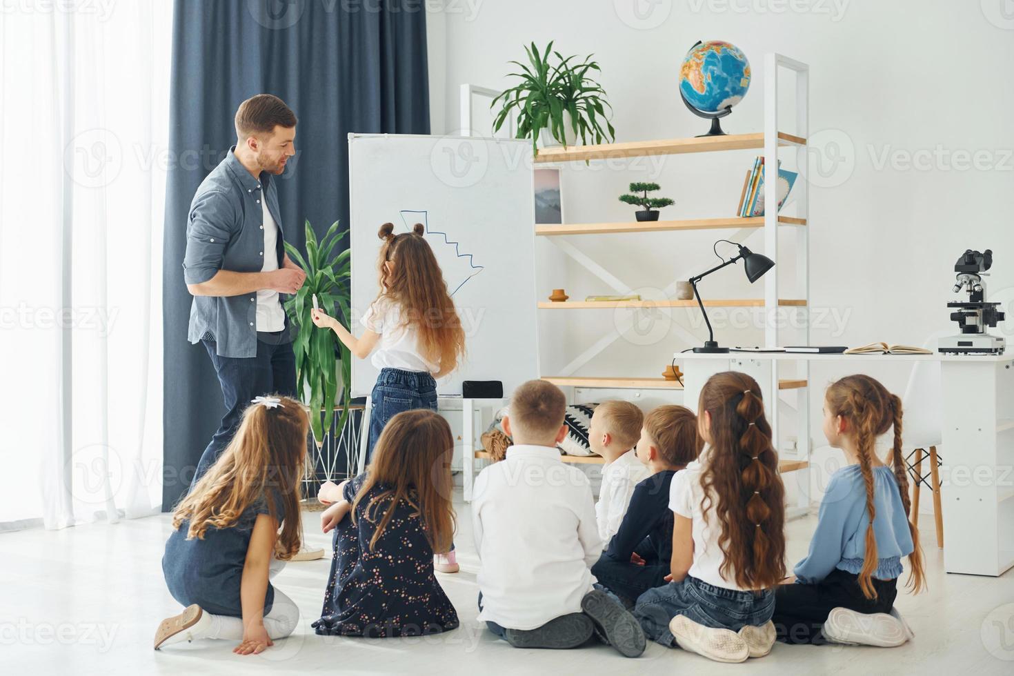 escrevendo no quadro. grupo de alunos de crianças em sala de aula na escola com professor foto