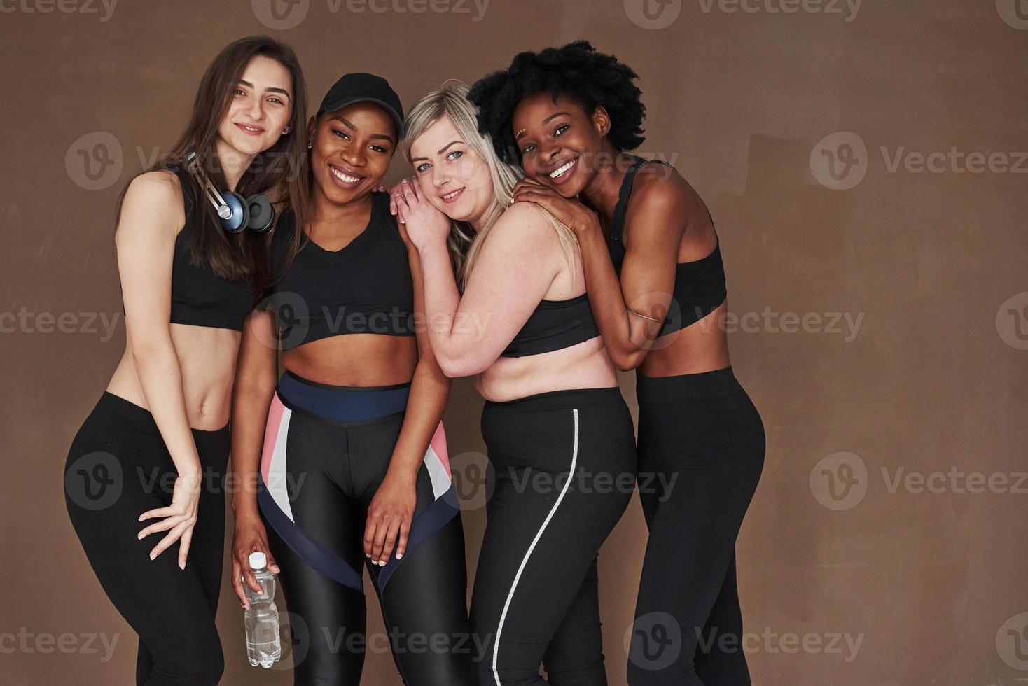 gostando de estar junto. grupo de mulheres multiétnicas em pé no estúdio contra fundo marrom foto