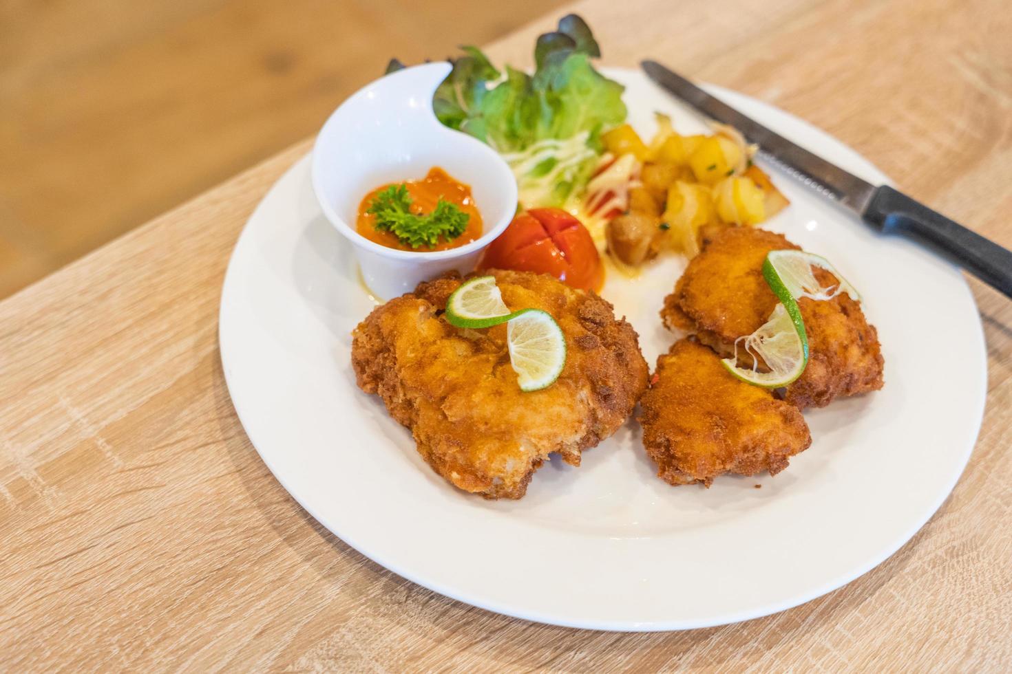 foco seletivo, bife de peixe frito com batata grelhada em chapa branca na mesa de madeira, dois pedaços de bacalhau empanado em um prato com batatas fritas, peixe e batatas fritas foto