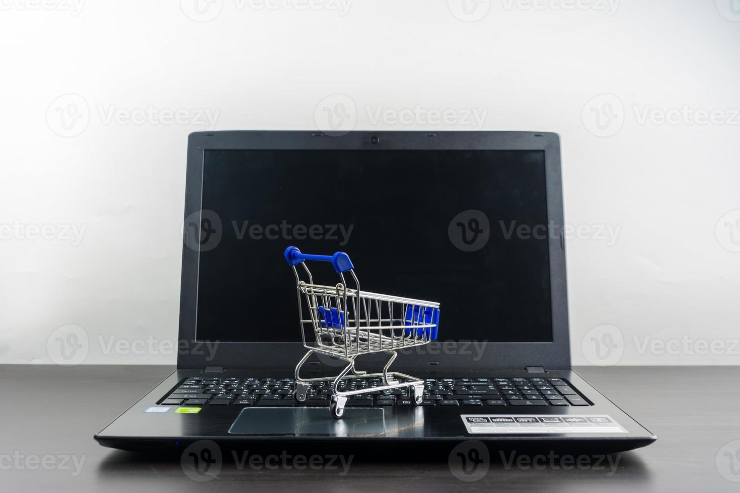 tela em branco do notebook do computador com carrinho de compras na mesa de madeira foto