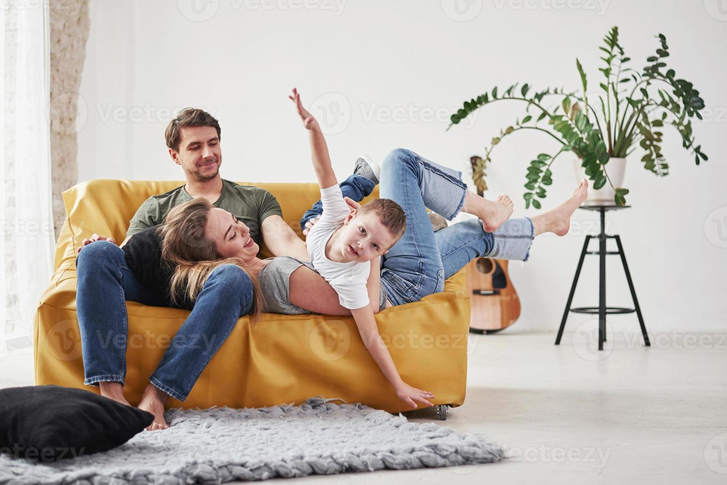 mãos nas laterais como um avião. família feliz se diverte no sofá amarelo na sala de sua nova casa foto