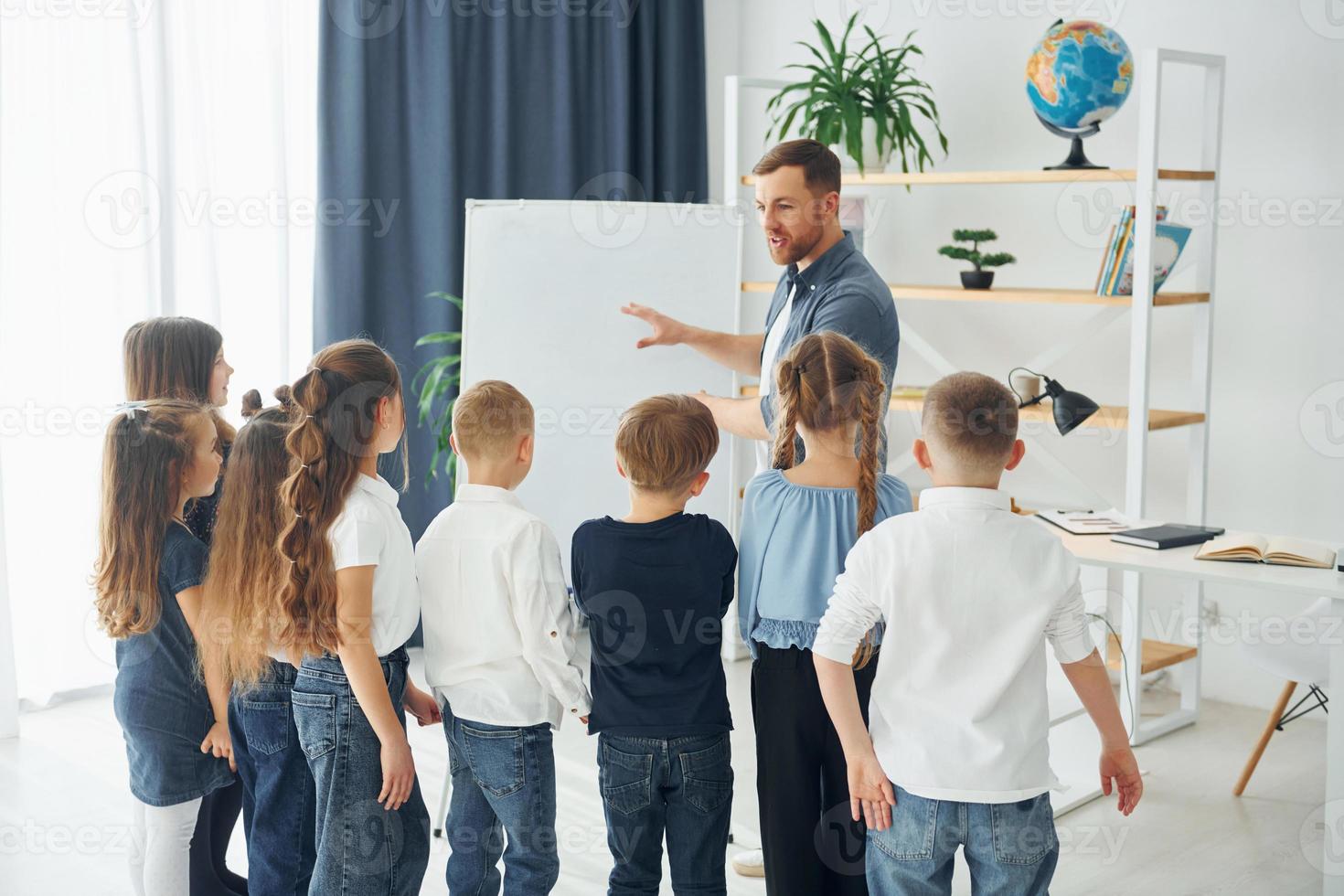 explicando a lição e usando o quadro. grupo de alunos de crianças em sala de aula na escola com professor foto