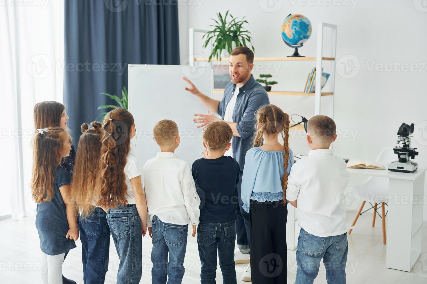 explicando a lição e usando o quadro. grupo de alunos de crianças em sala de aula na escola com professor foto