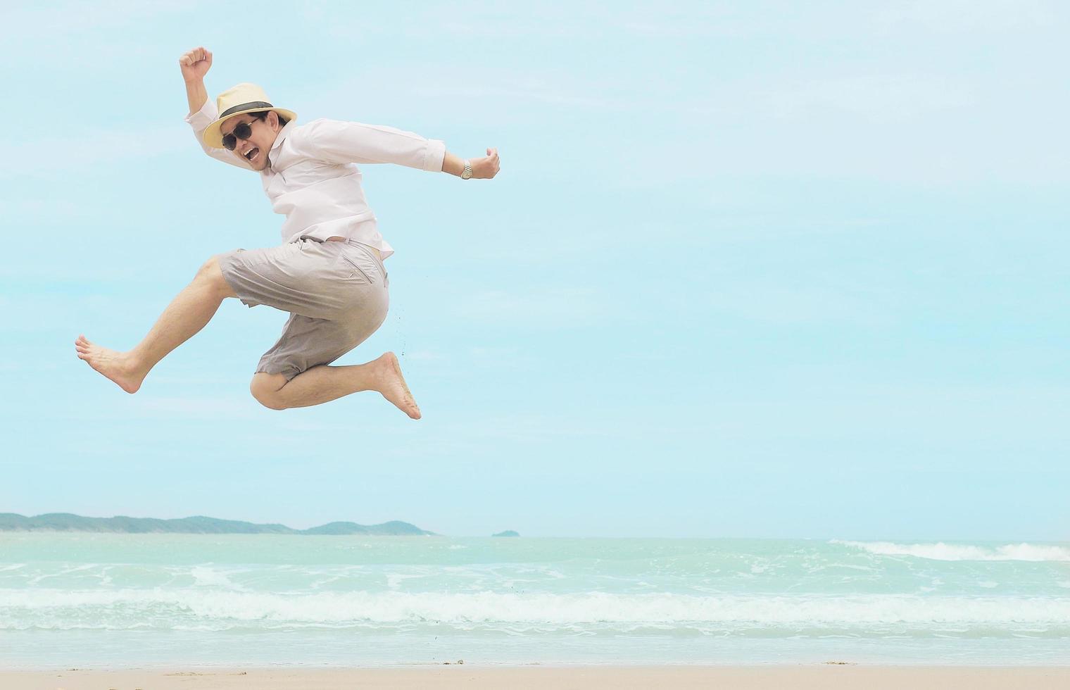 homem pula feliz durante as férias na praia do mar da tailândia foto