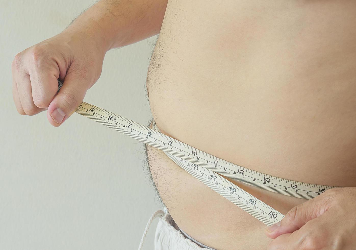 um homem aperta a fita métrica em torno de sua barriga gorda, conceito de obesidade foto