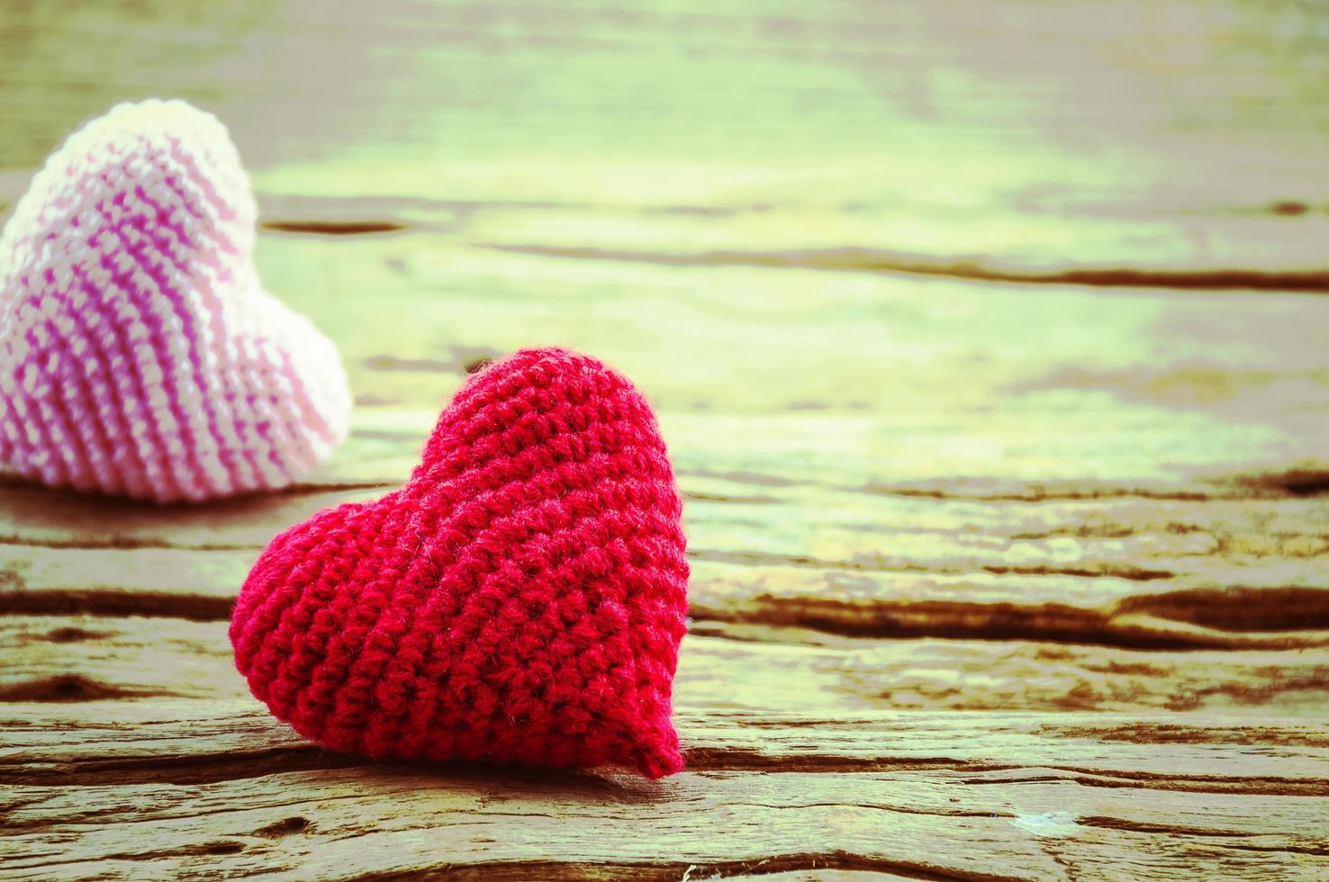 casal de coração de crochê em vermelho e rosa sobre fundo de madeira. foto é focada no coração vermelho.