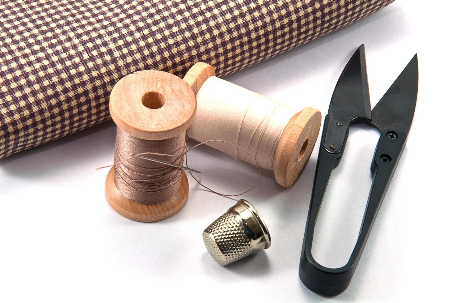 dedal, agulha, carretéis e tesoura com pano para costura em fundo branco foto