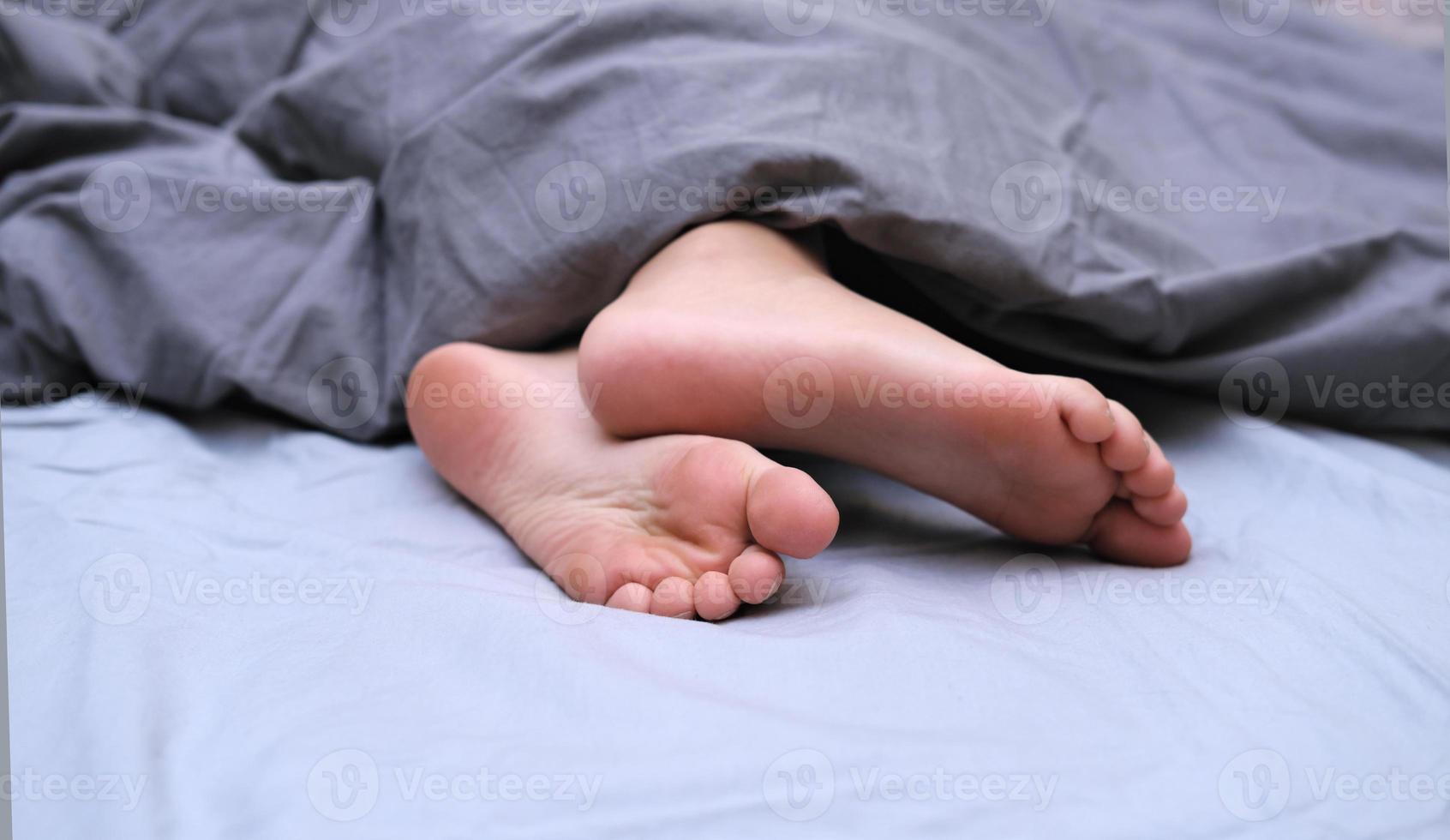 dedos dos pés da menina cobertos com lençol. vista de corte de uma garota na cama foto