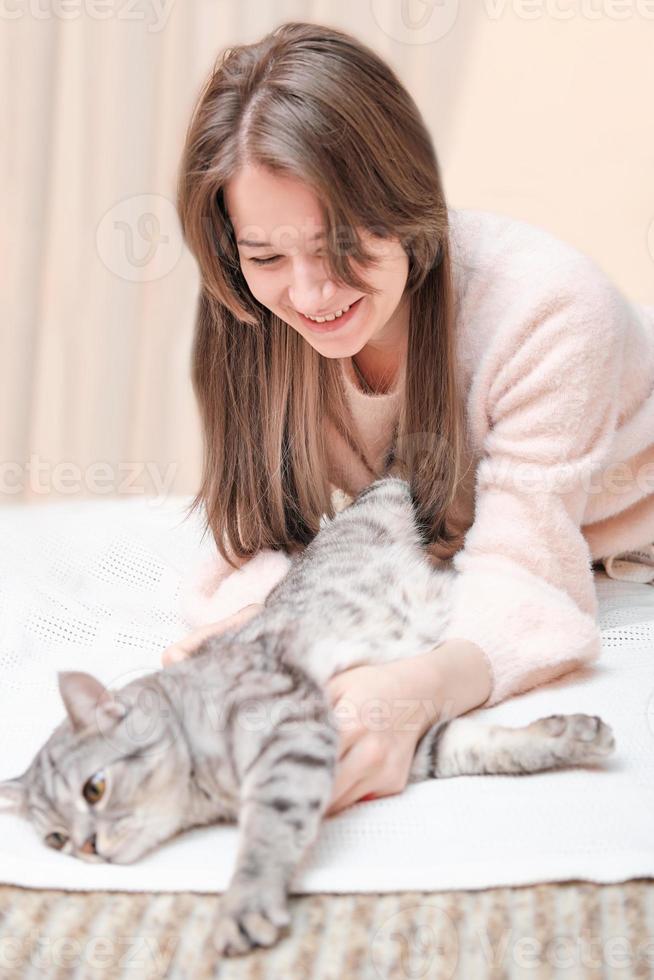 jovem brincando com seu gato deitado em uma cama. acariciando animal de estimação gentilmente, amizade e amor. foto