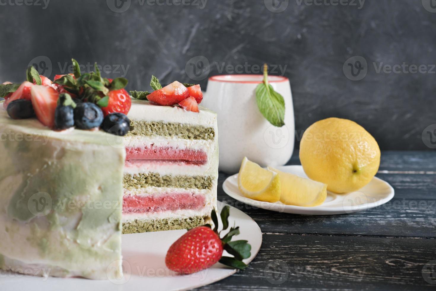 bolo de matcha e morango em camadas e uma xícara de chá com limão e hortelã. festa de aniversário. comida de férias. bolo caseiro vegetariano com ingredientes superalimentos. foto