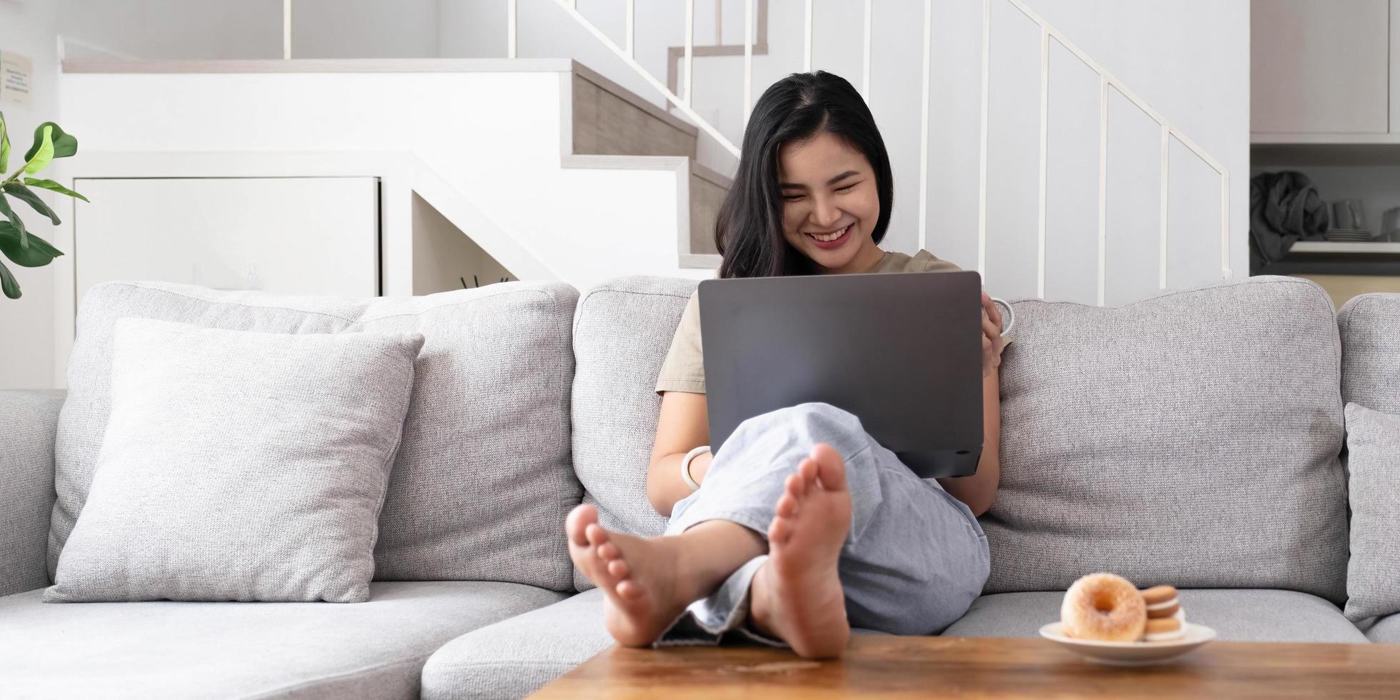 jovem asiática olhando laptop rindo com boas notícias ou voucher de desconto para compras on-line em casa. foto