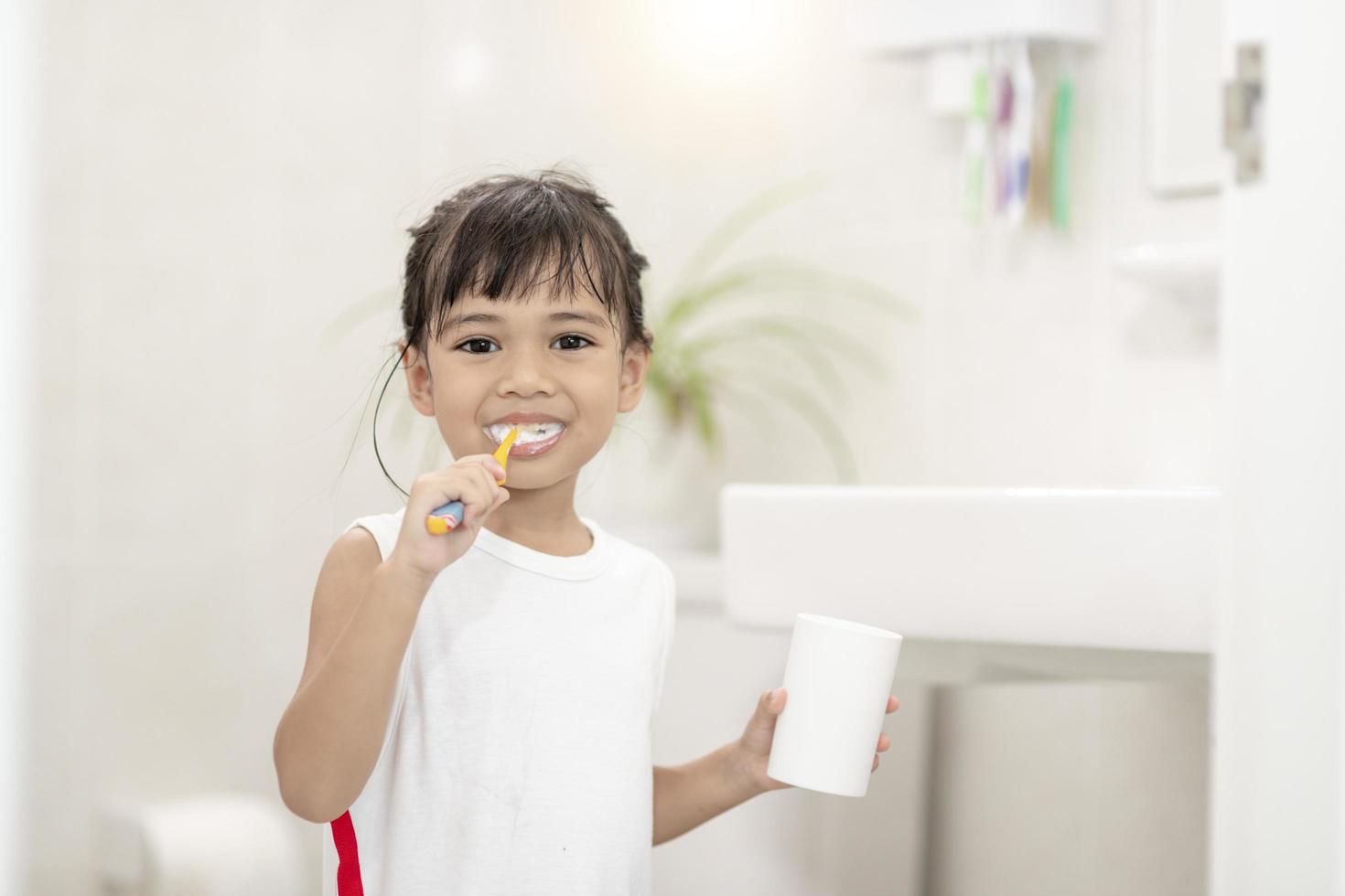 menina bonitinha limpando os dentes com uma escova de dentes no banheiro foto