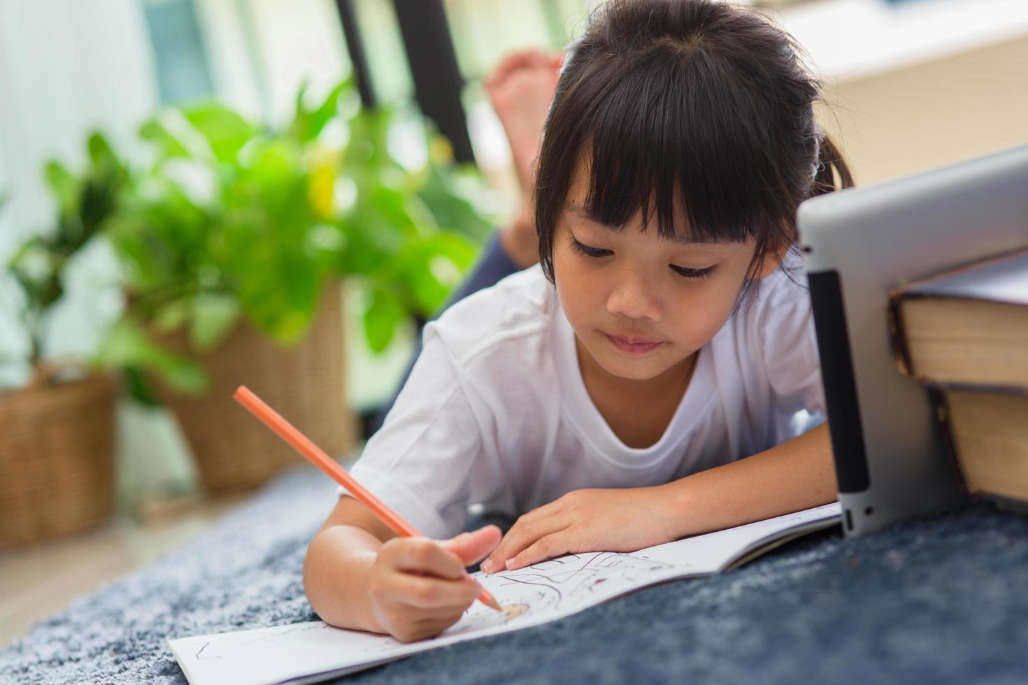 retrato de criança pré-escolar usando tablet para sua lição de casa, foco suave de criança fazendo lição de casa usando tablet digital pesquisando informações na internet, e-learning ou conceito de educação escolar em casa foto