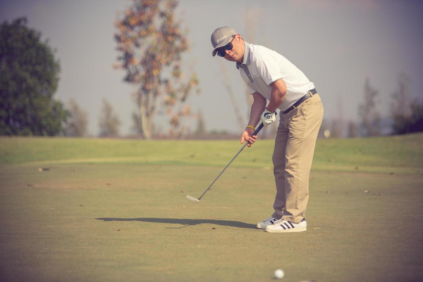 jogador de golfe no putting green batendo bola em um buraco. foto