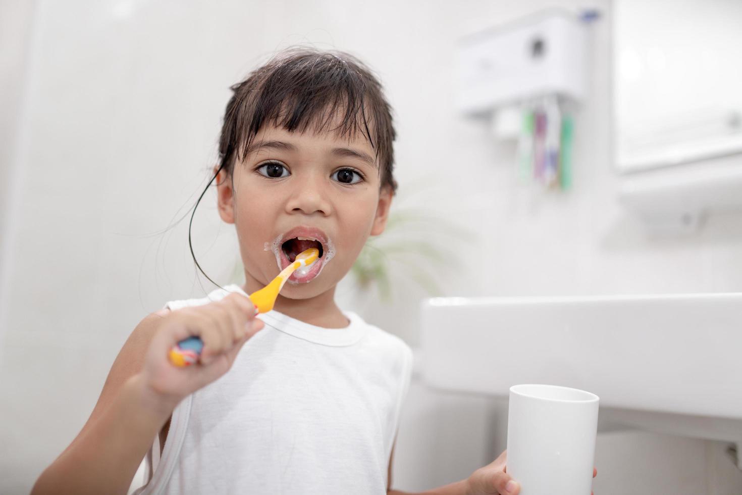 menina bonitinha limpando os dentes com uma escova de dentes no banheiro foto