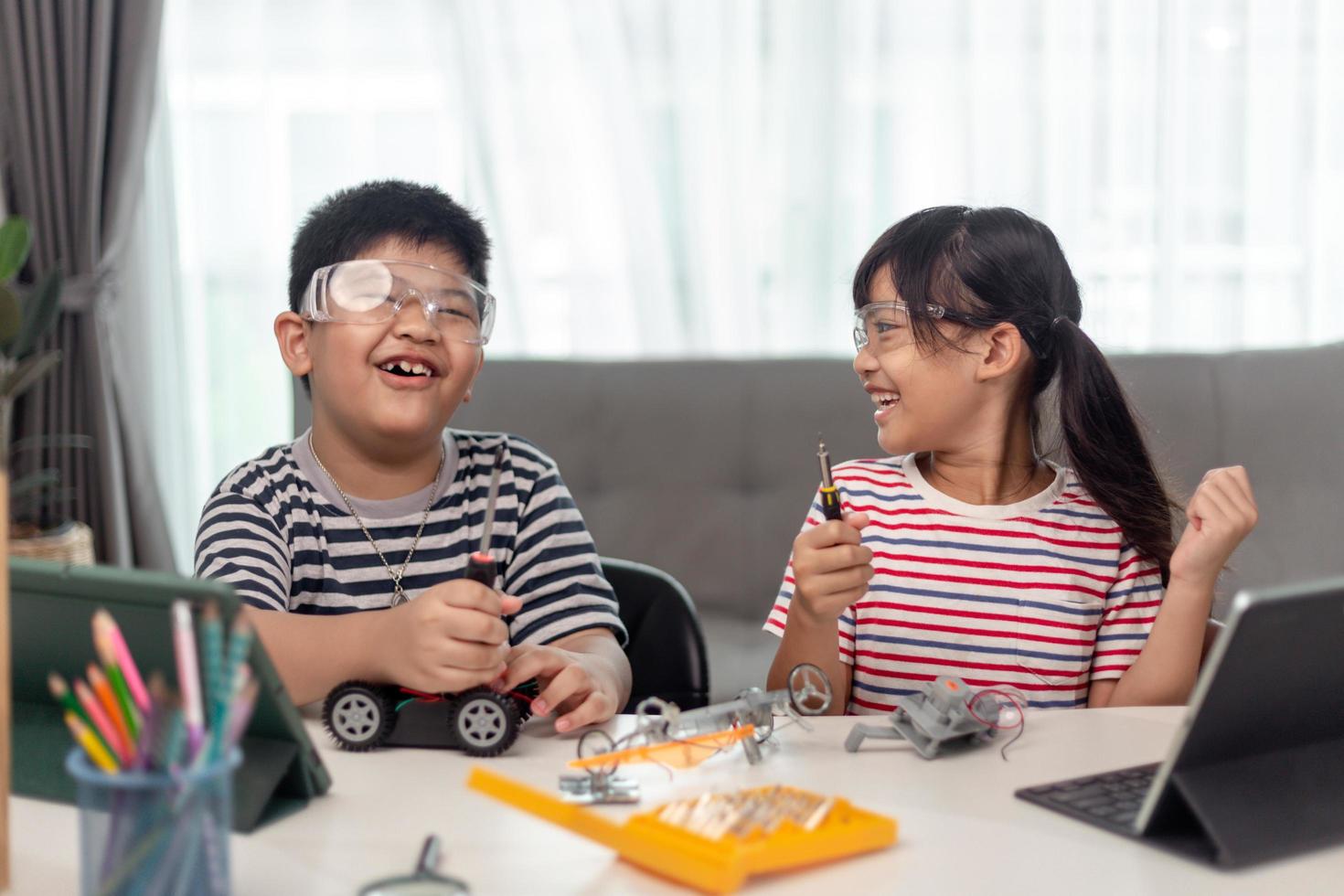 duas crianças asiáticas se divertindo aprendendo codificação juntas, aprendendo remotamente em casa, ciência da haste, educação escolar em casa, distanciamento social divertido, isolamento, novo conceito normal foto