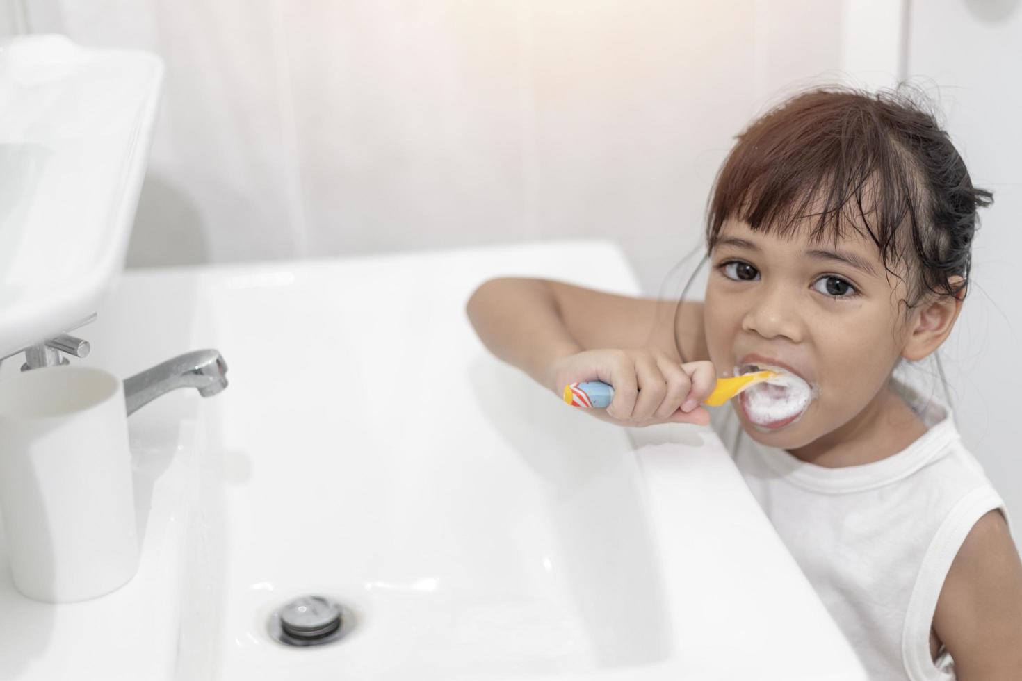 menina bonitinha limpando os dentes com uma escova de dentes no banheiro foto