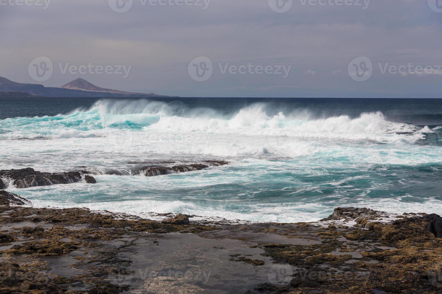 ondas oceânicas turbulentas com espuma branca batem nas pedras costeiras foto