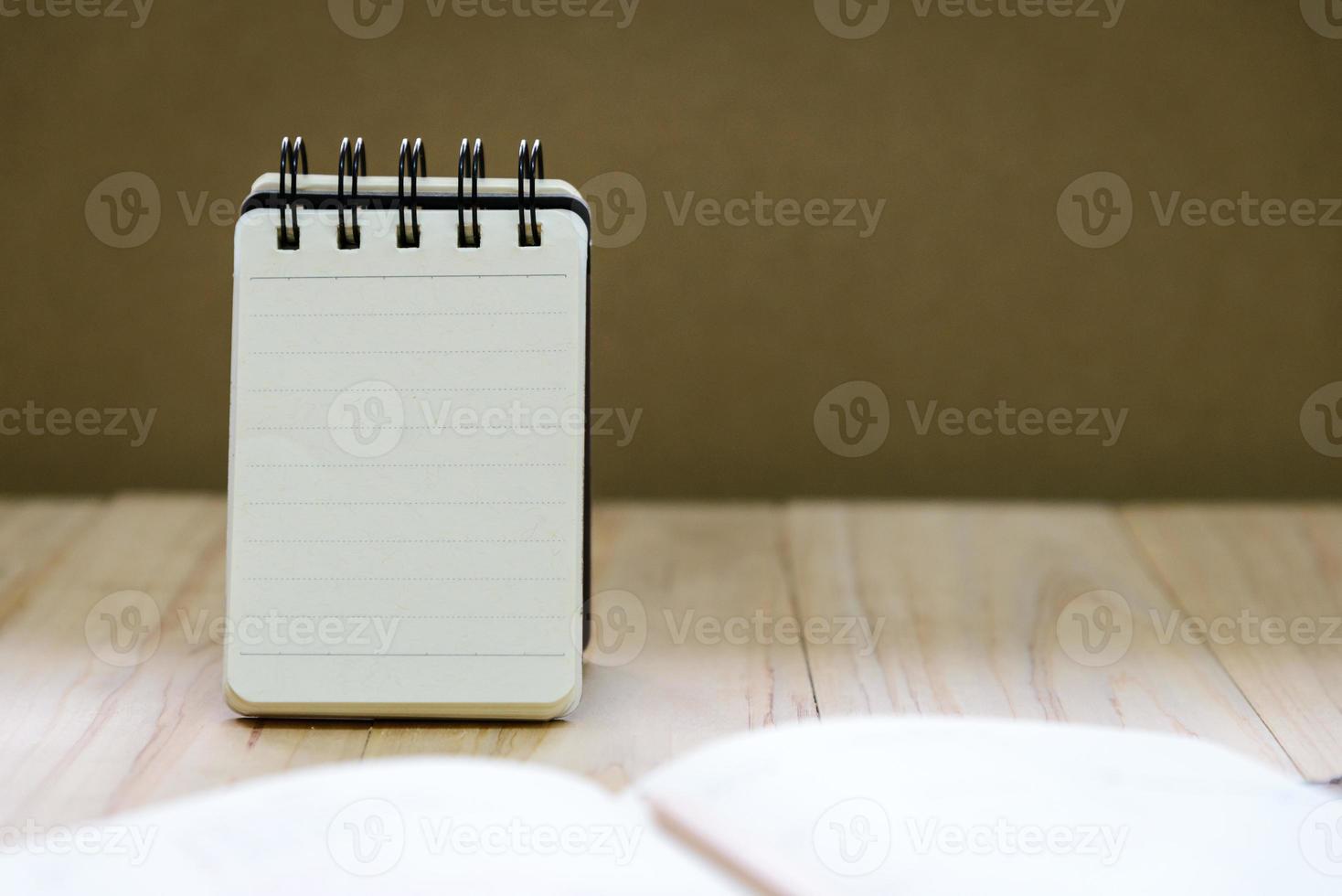 papel de caderno pequeno ou suporte de bloco de notas para escrever informações com lápis e livro na mesa de madeira foto
