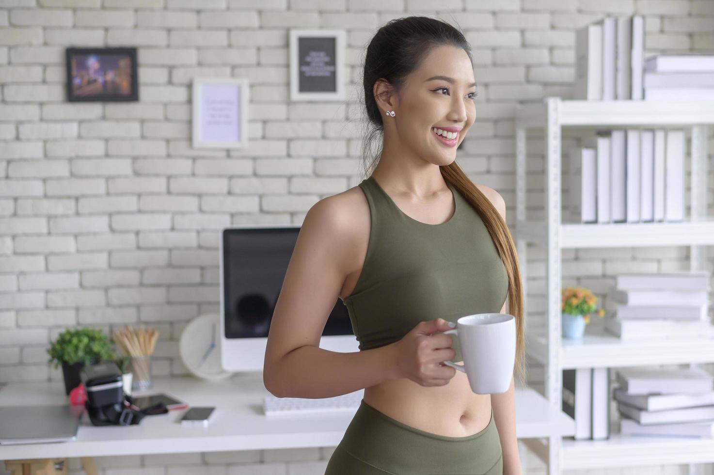 mulher jovem fitness em roupas esportivas tomando uma xícara de café depois de se exercitar em casa, saudável e estilos de vida. foto