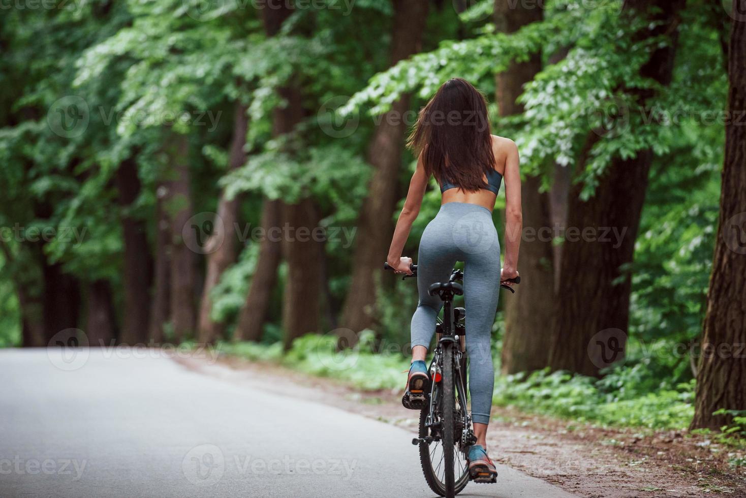 energia e vitalidade humana. ciclista feminina em uma bicicleta na estrada de asfalto na floresta durante o dia foto