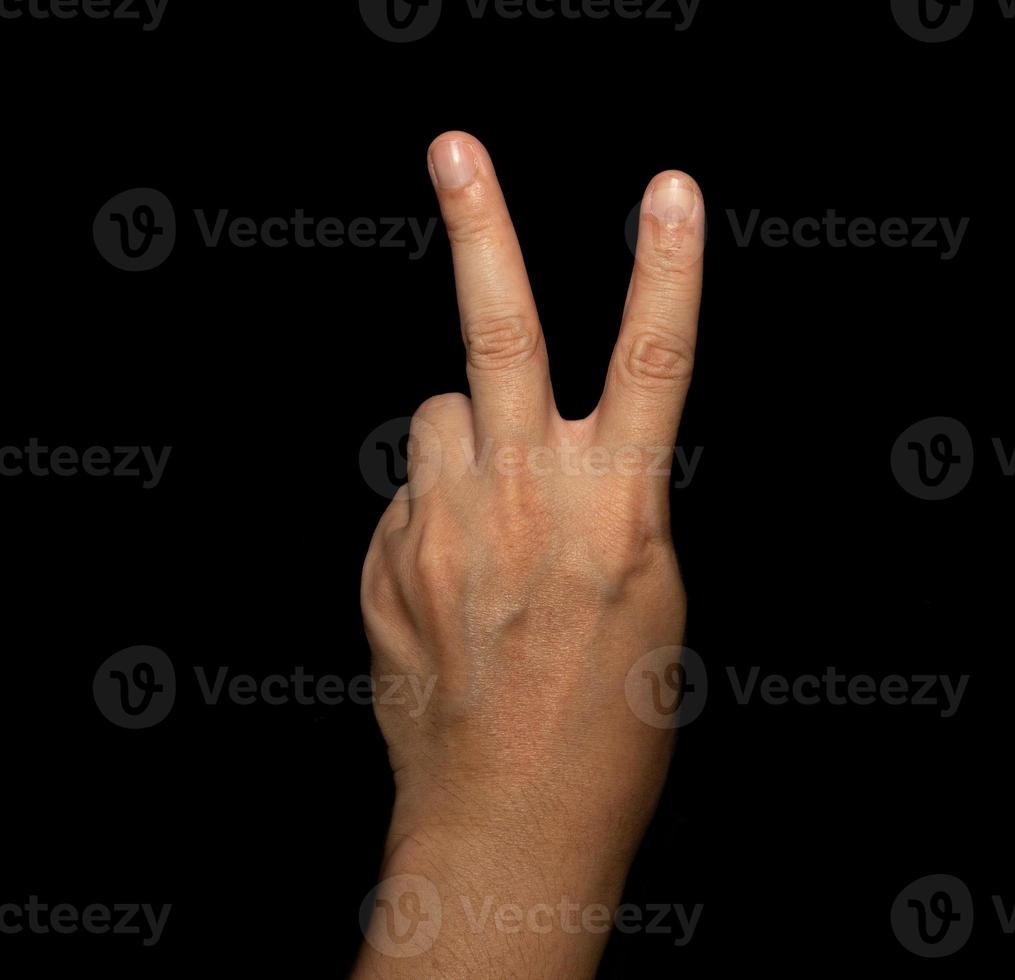 a mão do homem que segura dois dedos é um sinal de av, que significa vitória. ou ainda significa paz e desprezo por desafios em fundo preto foto