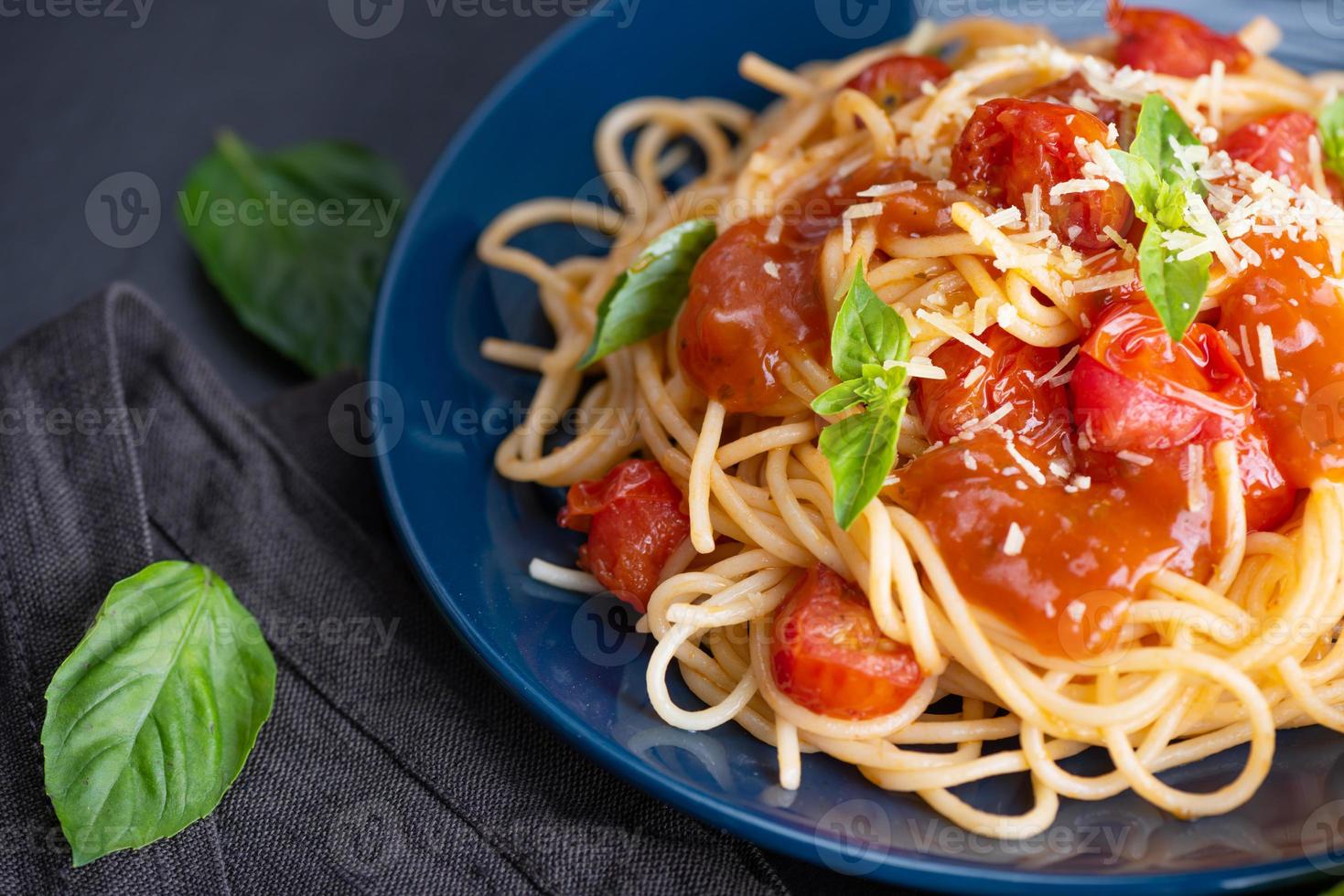 saboroso e apetitoso macarrão espaguete italiano clássico com molho de tomate, queijo parmesão e manjericão no prato e ingredientes para cozinhar macarrão na mesa escura. foto