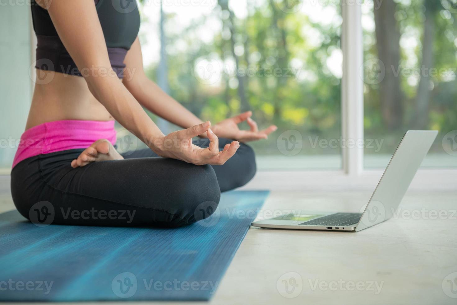 mulher desportiva praticando ioga, fazendo exercício ardha padmasana, meditando em pose de lótus, malhando, vestindo roupas esportivas, assistindo tutorial em vídeo de fitness on-line no laptop, fazendo exercícios em casa sentado foto