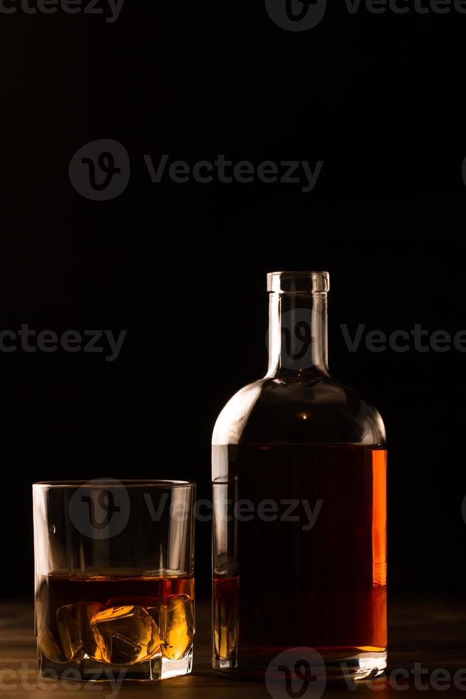 copo de uísque com gelo e garrafa na mesa de madeira. foto