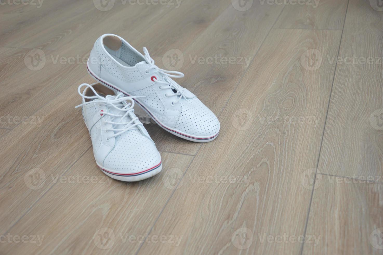 tênis de couro branco em um piso de madeira marrom. inserções macias de esfregar calos nos calcanhares. calçado de moda. lugar para texto. foto