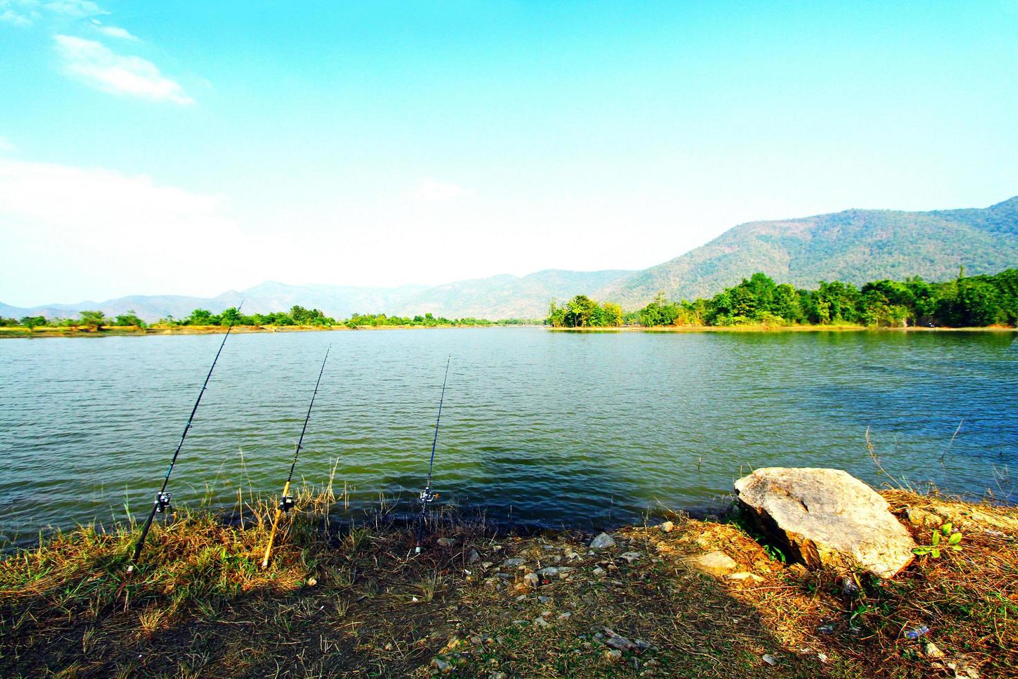 três varas de pesca com belo lago, montanhas e fundo de céu azul. ferramenta para pegar peixes e conceito de esporte foto