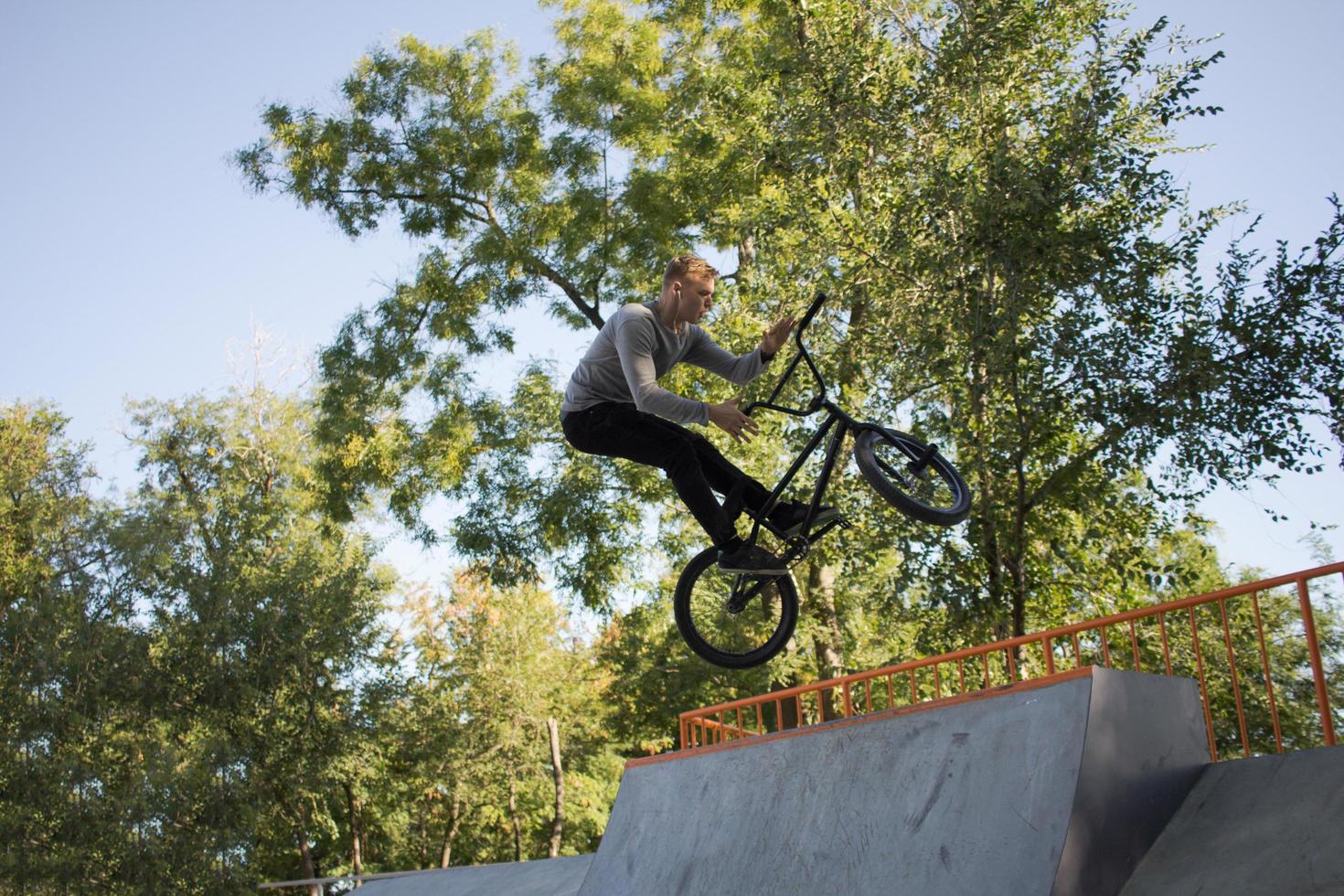 bmx rider treinando e fazendo truques na street plaza, bicyxle stunt rider em coccrete skatepark foto