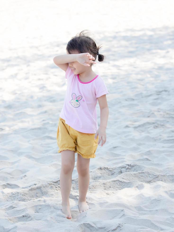 positiva encantadora menina asiática de 4 anos de idade, criança pré-escolar brincando na praia de areia em lindo dia ensolarado no horário de verão. foto