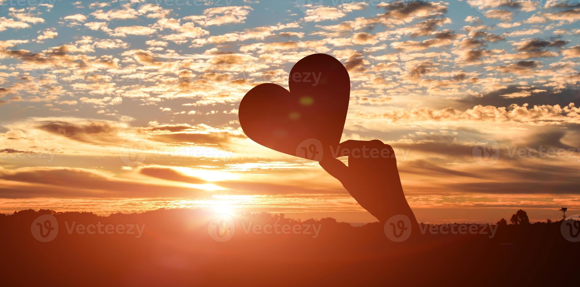 silhueta de mãos segurando corações no fundo do céu por do sol. conceito de dia de amor foto