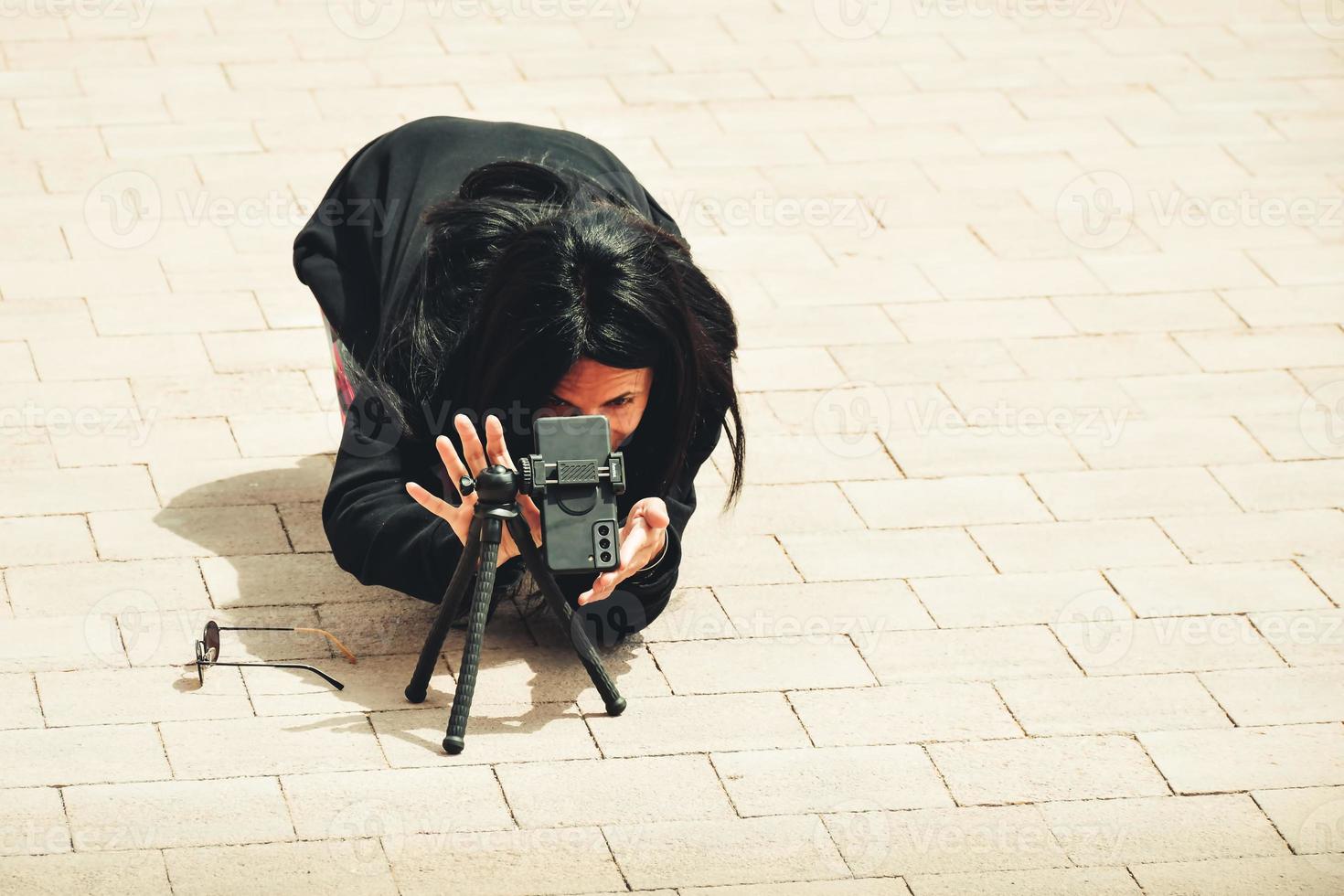 animado jovem morena caucasiana fotógrafo de viagens fotografar com smartphone em tripé ao ar livre em público no destino turístico foto