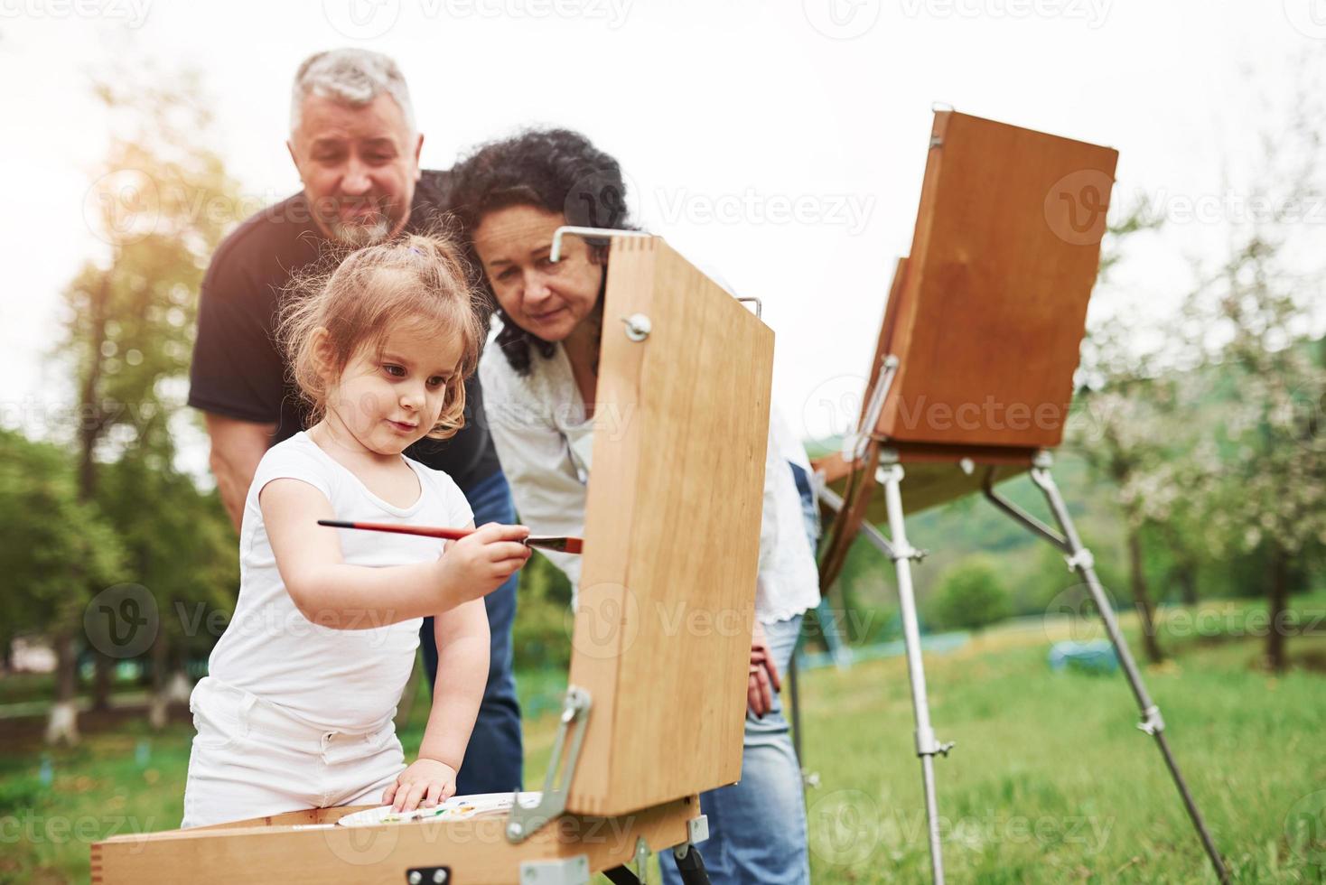 usando pincel de cor vermelha. avó e avô se divertem ao ar livre com a neta. concepção de pintura foto