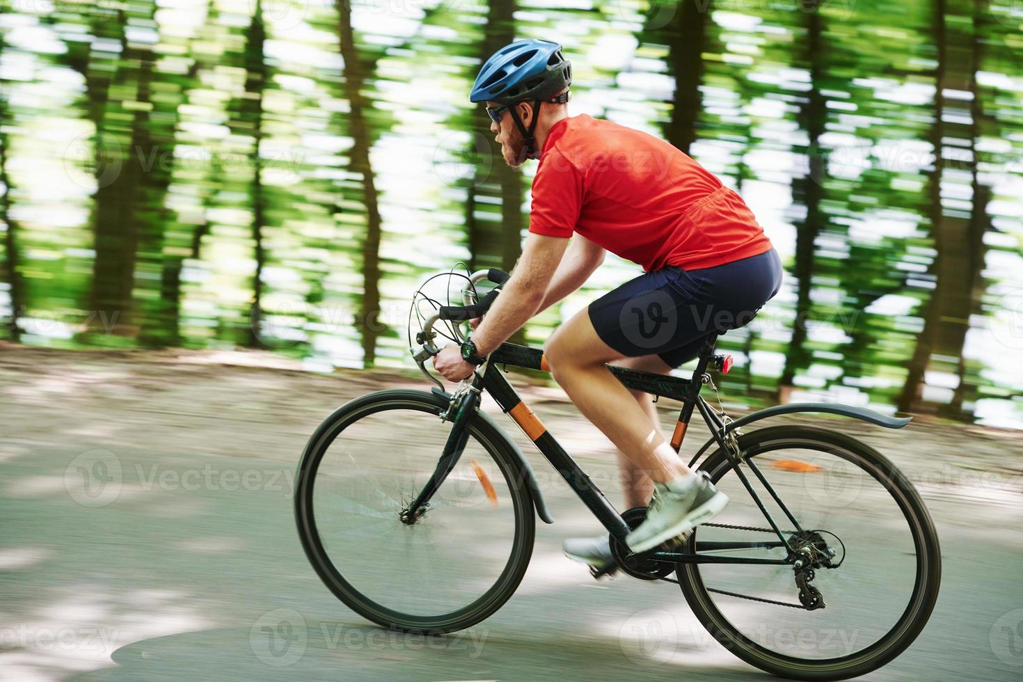fundo desfocado. ciclista de bicicleta está na estrada de asfalto na floresta em dia ensolarado foto