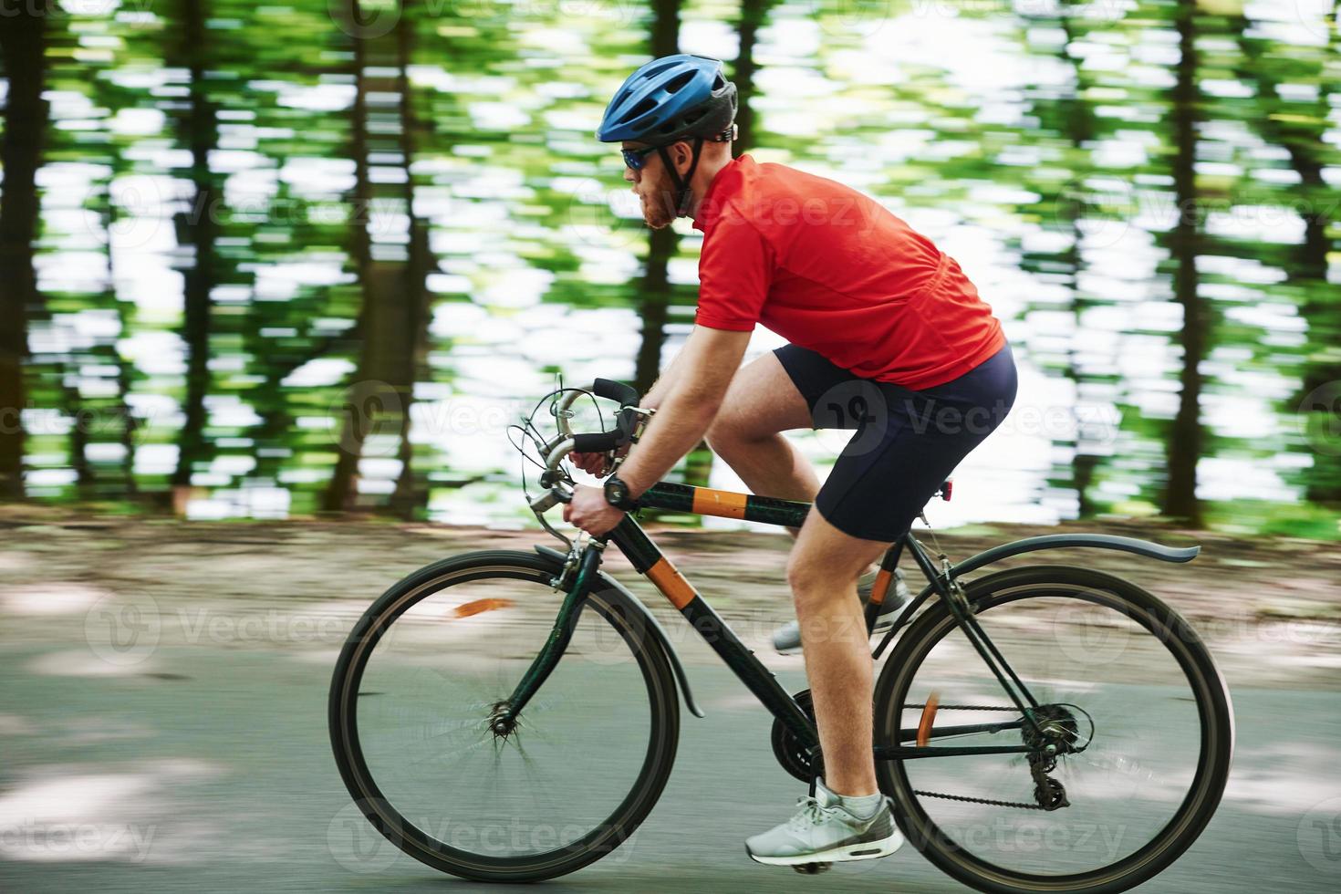 concepção de estilo de vida saudável. ciclista de bicicleta está na estrada de asfalto na floresta em dia ensolarado foto