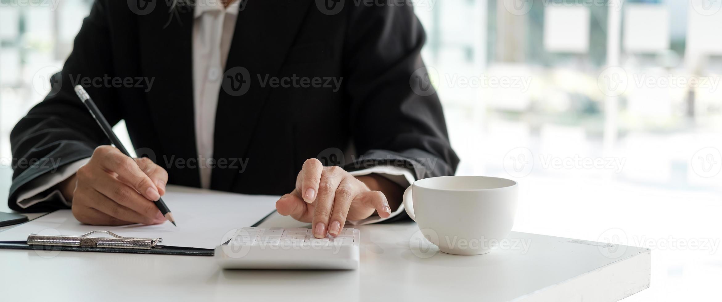 foto de corte de mão de mulher contadora na calculadora e escrevendo uma nota para fazer relatório financeiro ou lucro anual da empresa na mesa, trabalho de guarda-livros