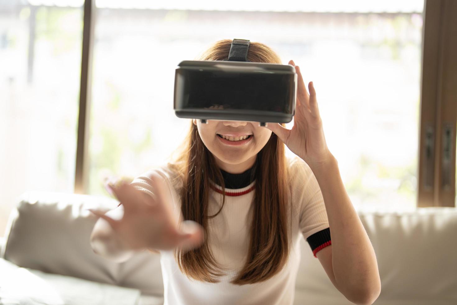 excitar a mulher asiática jogando online com óculos vr e controlador em sua casa foto