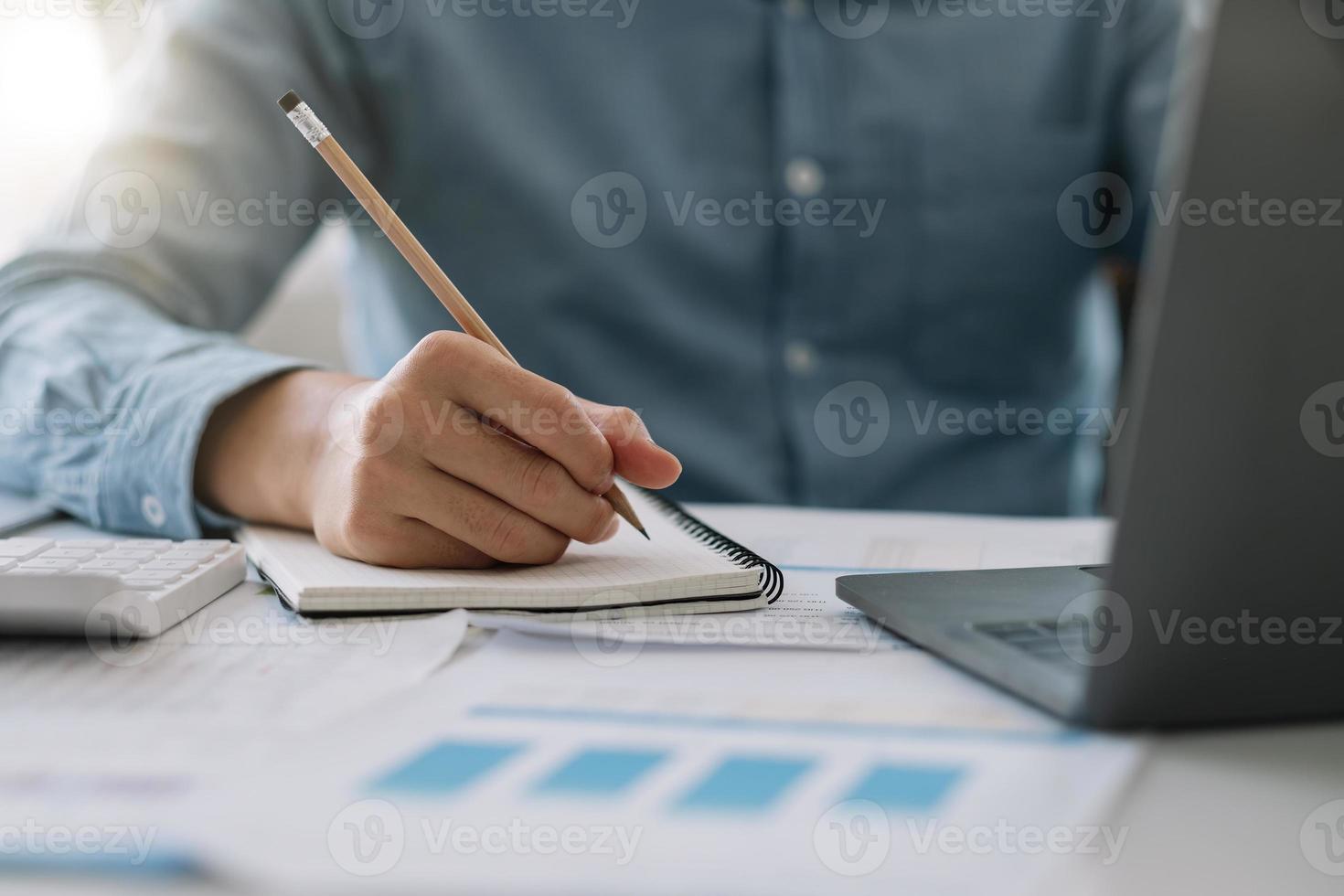 Feche a mão do homem de negócios tomando nota enquanto estiver usando calculadoras e computador portátil para relatório financeiro. conceito de contabilidade foto