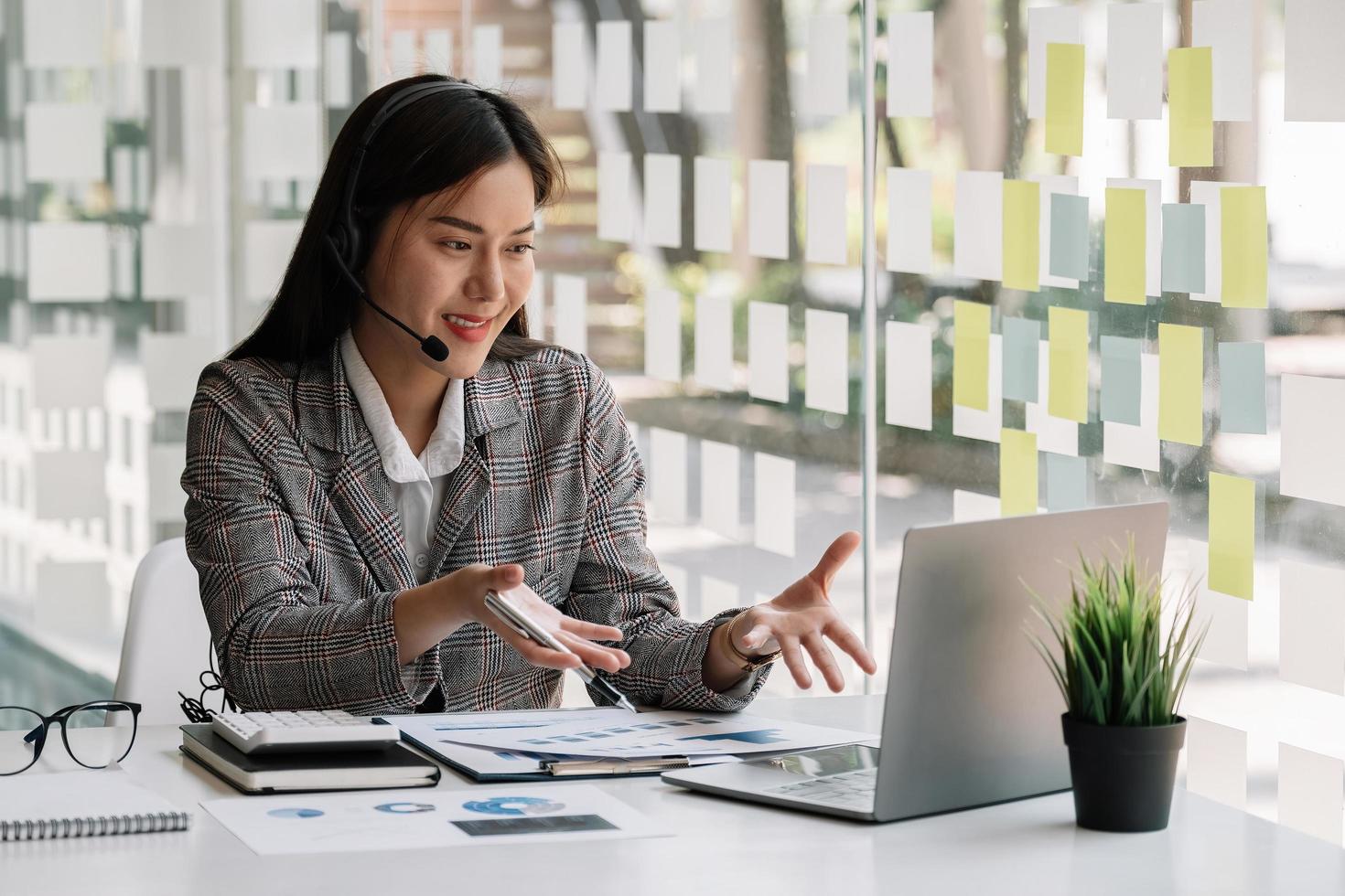 mulher asiática usando fones de ouvido, gostando de assistir webinar educacional no laptop. sorrindo jovem empresário de raça mista segurando vídeo chamada com parceiros de clientes. foto