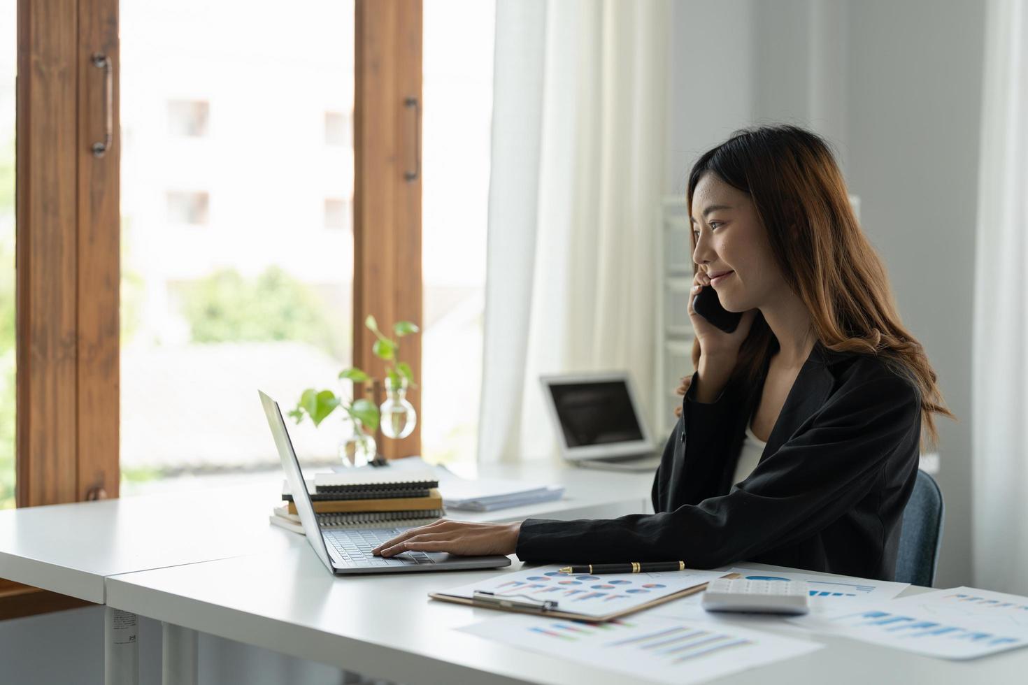 empresária asiática falando no celular trabalhando no laptop para finanças no escritório moderno. foto