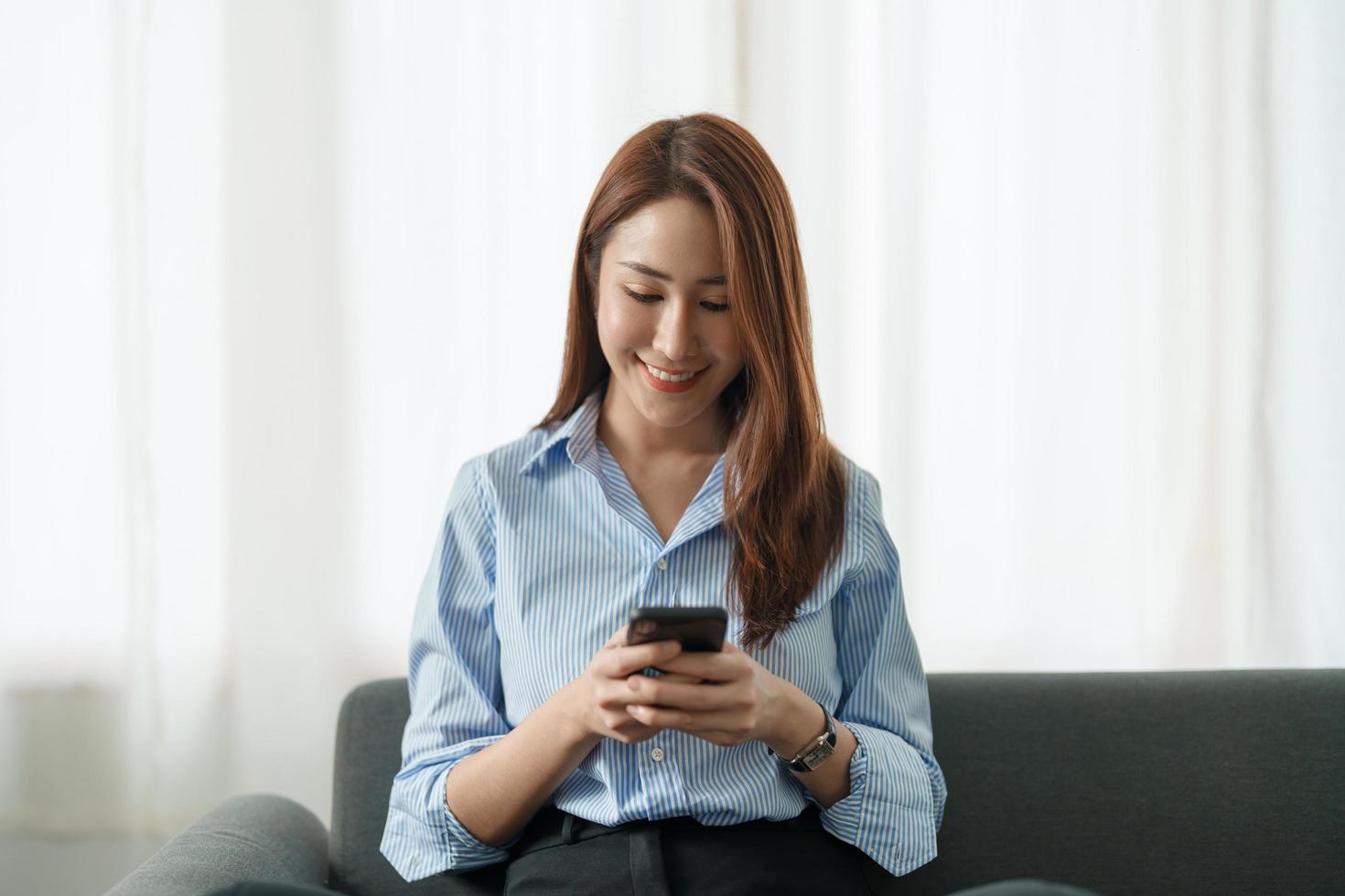 menina asiática feliz segurando o celular usando o dispositivo smartphone em casa. jovem blogueira latina sorridente assinando novas mídias sociais, comprando na internet, encomendando produtos on-line em aplicativos. mão de perto foto