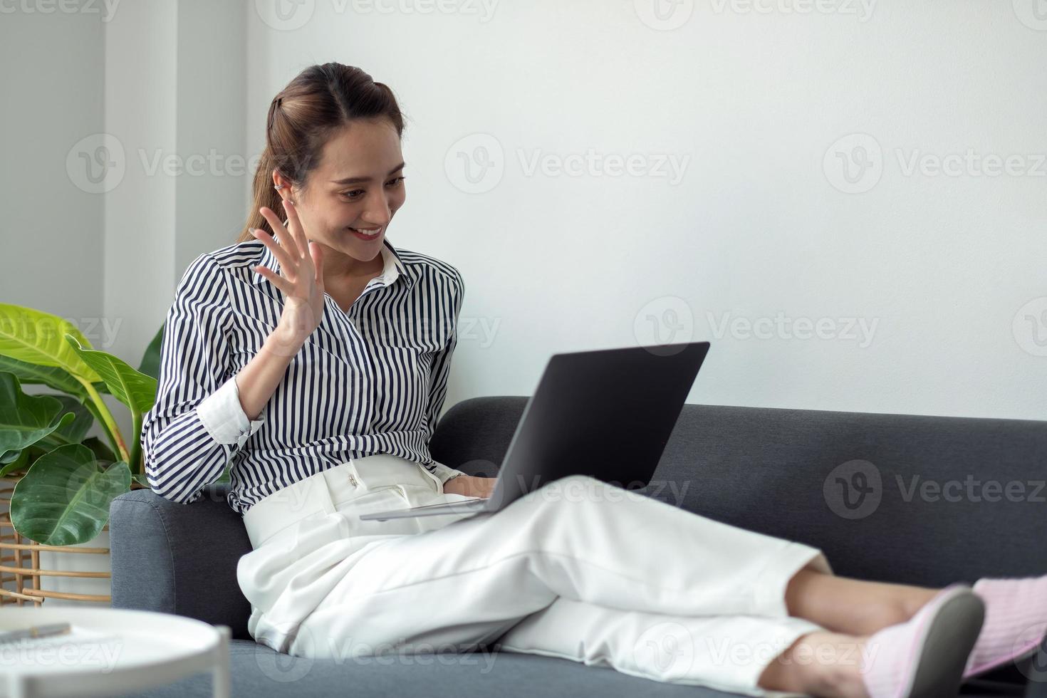 conceito de tecnologia, lazer e pessoas - mulher sorridente feliz com computador portátil tendo bate-papo por vídeo e acenando com a mão em casa. foto