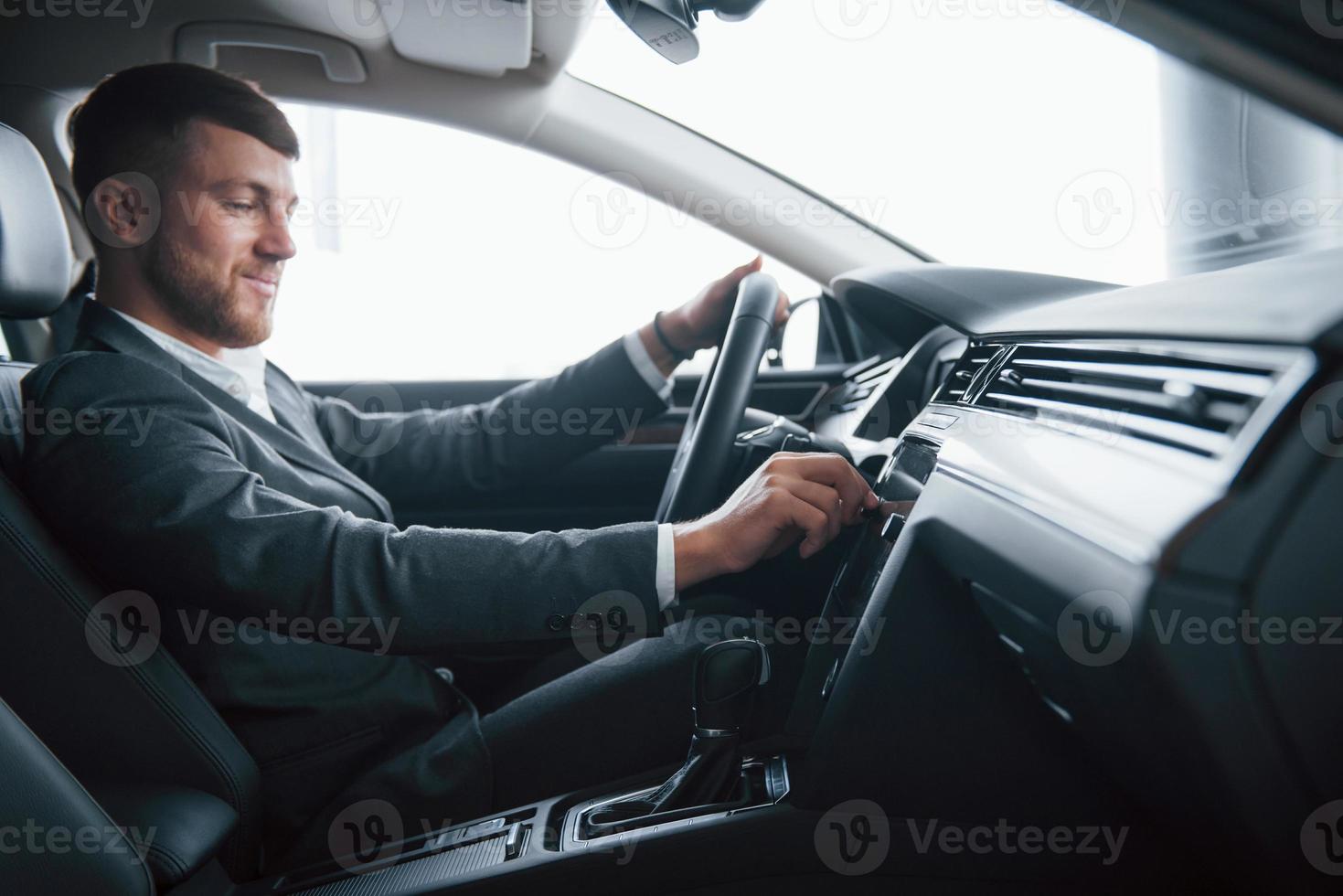 ligue a música. empresário moderno tentando seu carro novo no salão de automóveis foto