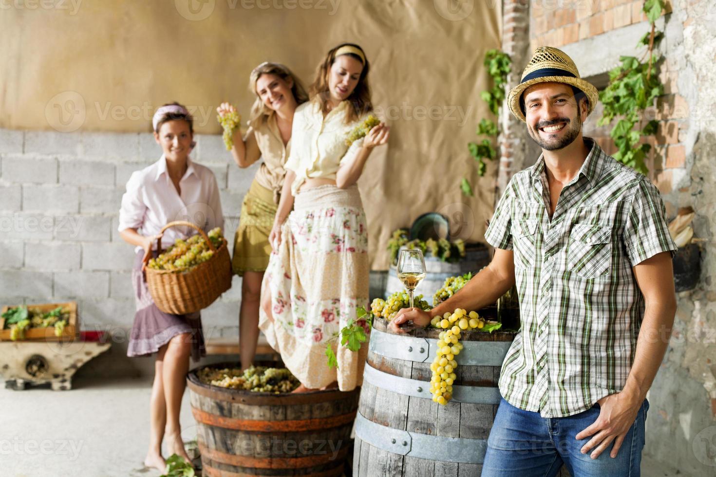 agricultor bebe vinho enquanto as mulheres batendo uvas foto