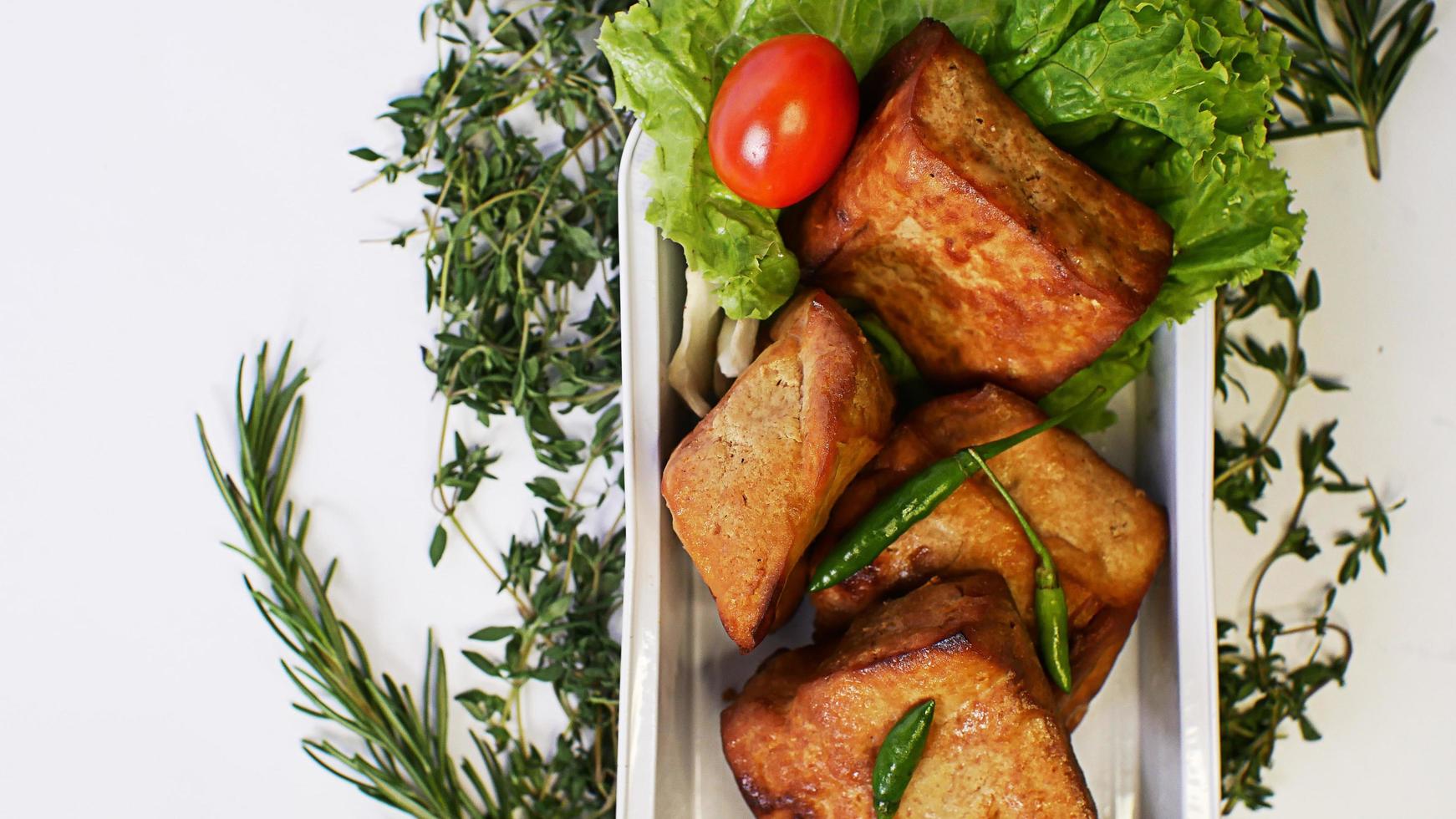 tofu frito, tomates pequenos e pimentões verdes junto com alface em um recipiente de alumínio, comida de rua indonésia em um fundo branco foto